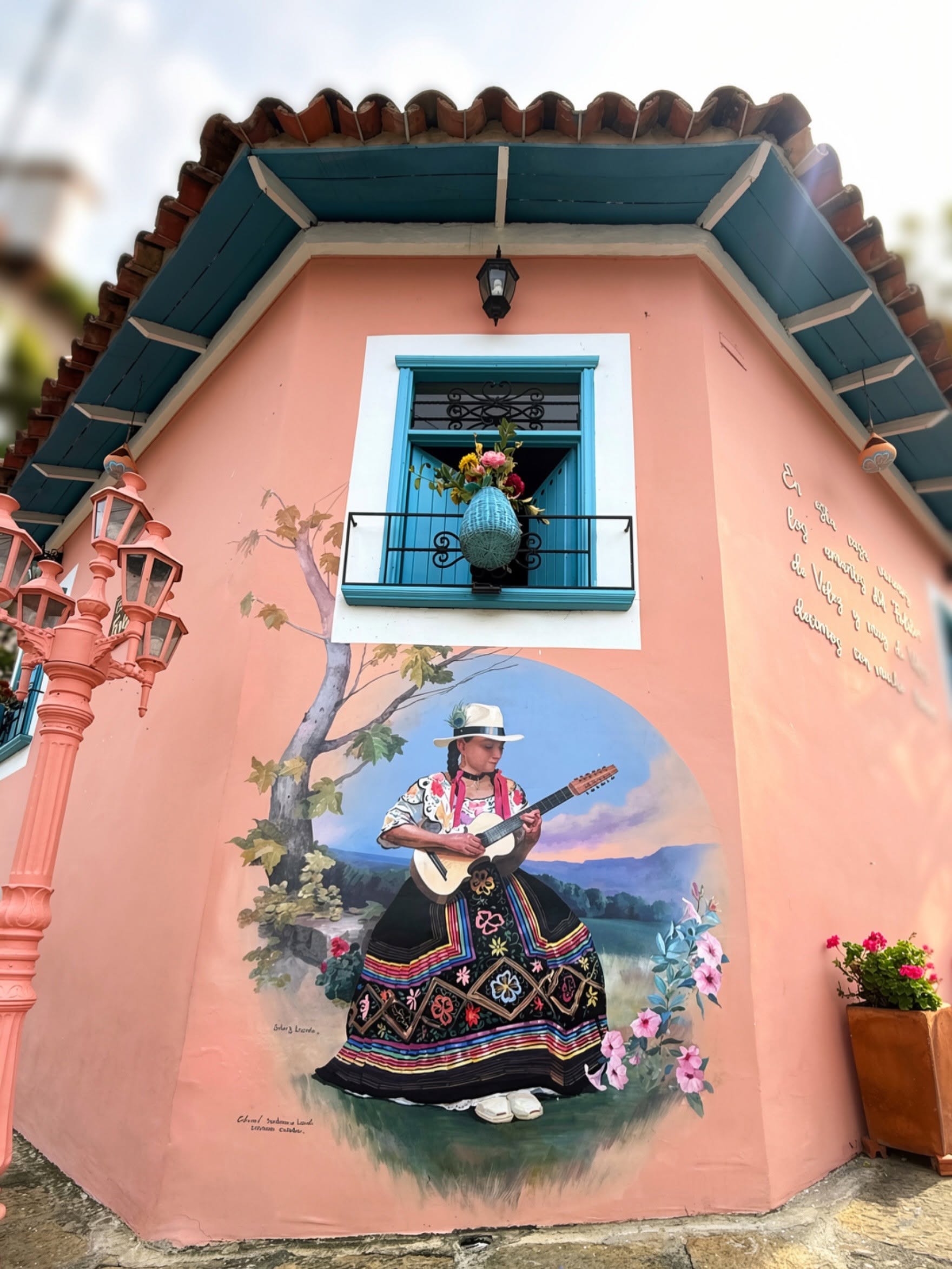 Mural de una mujer con traje típico veleño tocando el tiple, en una fachada coral de Vélez