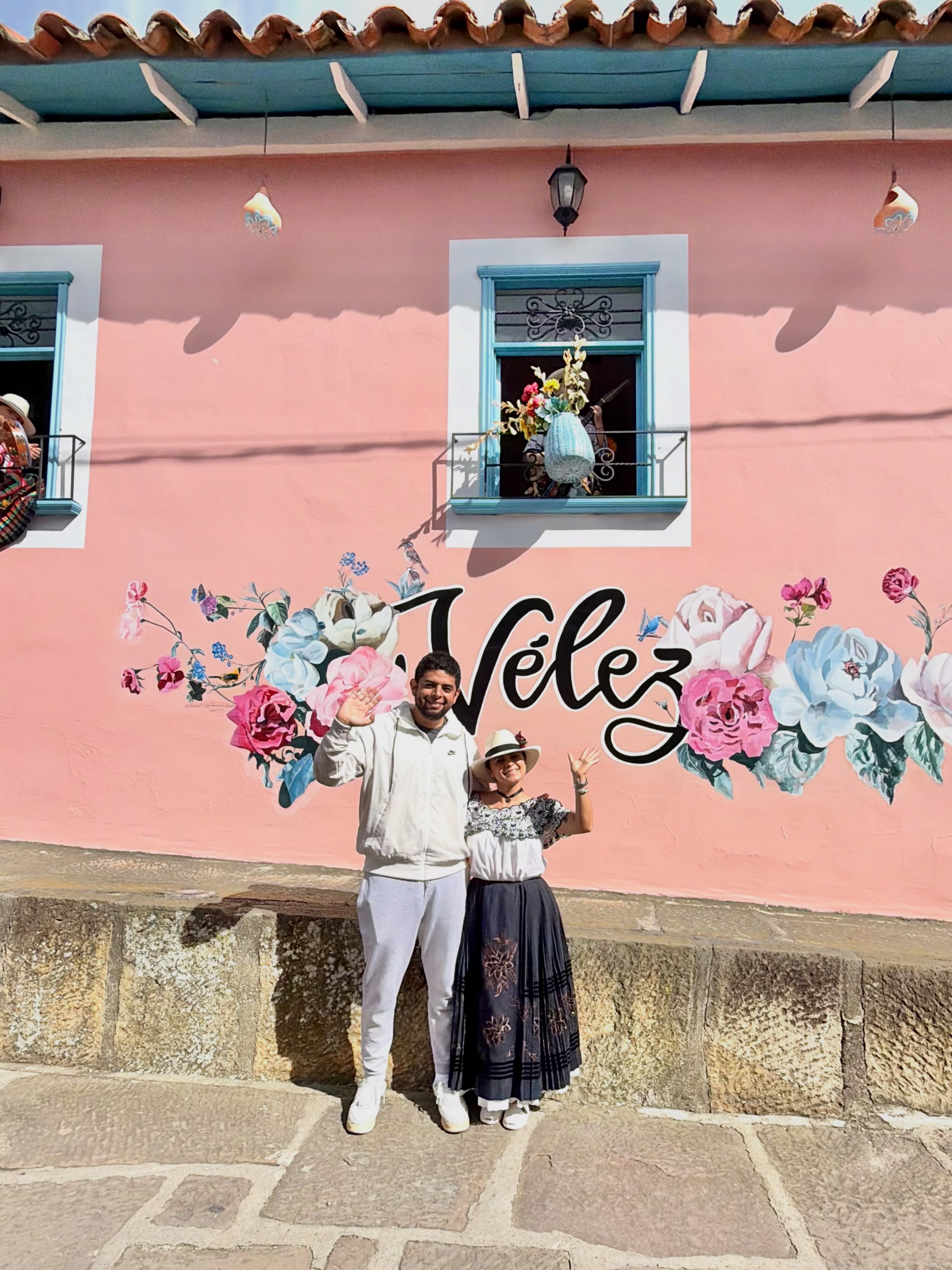 Pareja saludando frente al mural floral de Vélez